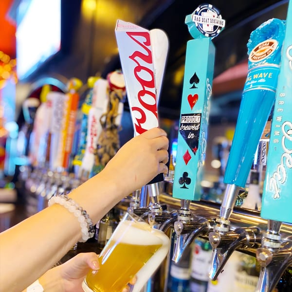 A hand pulls a Coors beer tap, filling a glass with golden beer at Born And Raised Centennial.
