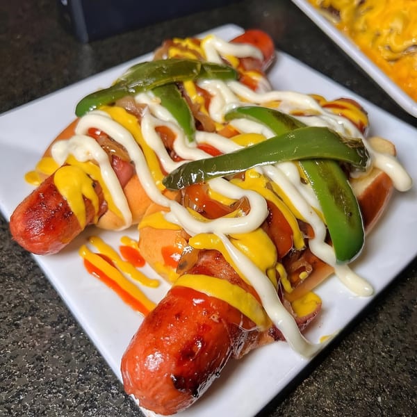 Two hot dogs with mustard, mayonnaise, grilled onions, and green peppers on a white plate.
