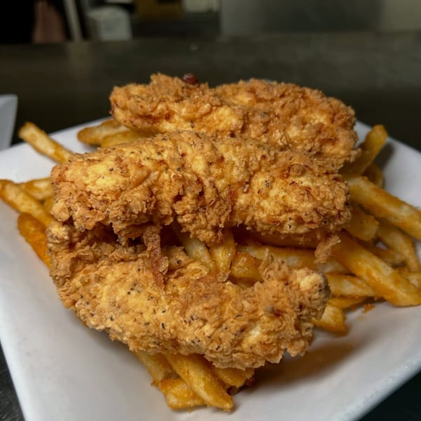Crispy, golden-brown chicken tenders with black pepper seasoning, served atop a bed of french fries.