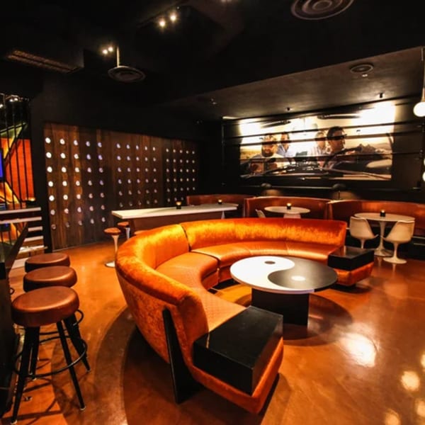 A sports bar interior with an orange curved sofa, yin-yang table, and a large screen.