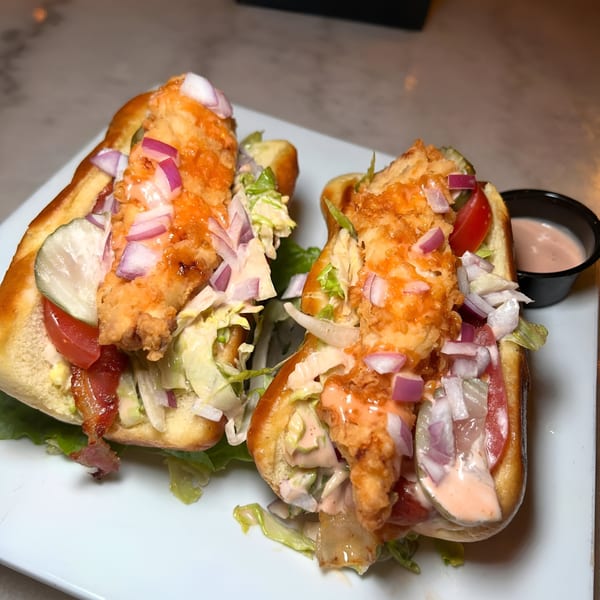 Two crispy chicken sandwiches with lettuce, tomato, pickles, red onion, and sauce on a white plate.