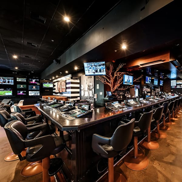 A long, dark bar with numerous screens showing sports, and bar stools with copper bases.