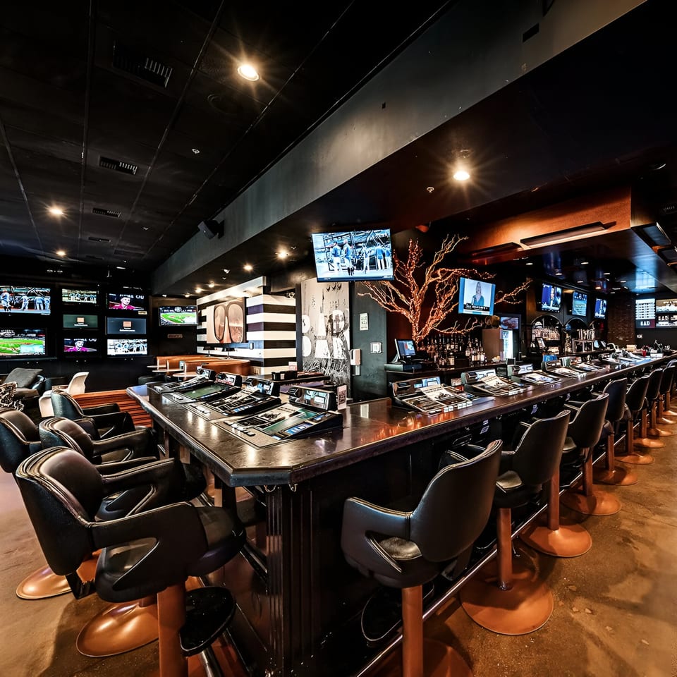 A long, dark bar with numerous screens showing sports, and bar stools with copper bases.