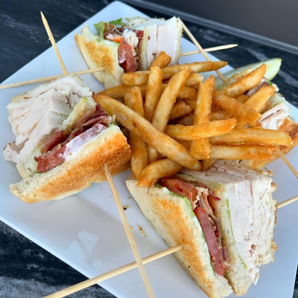 Born And Raised Centennial's turkey club sandwich with bacon, lettuce, tomato, and fries on a white plate.