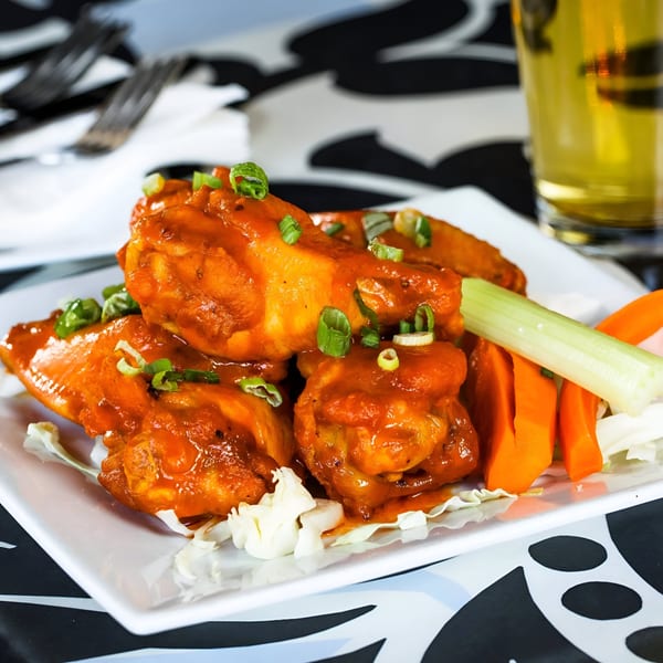 Born And Raised Centennial's buffalo wings, garnished with green onions, celery, and carrots, with a beer.