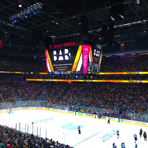 A packed T-Mobile Arena during a hockey game, with a large scoreboard displaying "BAR" and "T-Mobile Arena".