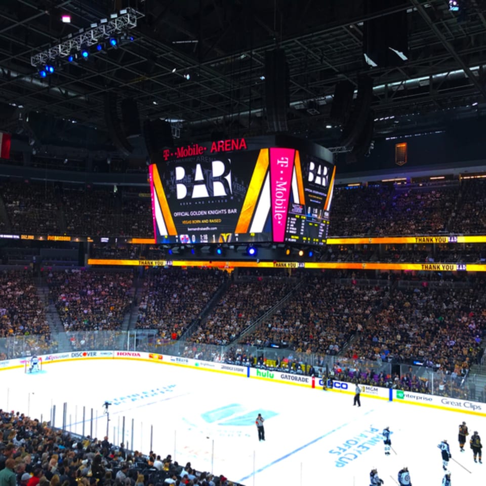 A packed T-Mobile Arena during a hockey game, with a large scoreboard displaying "BAR" and "T-Mobile Arena".